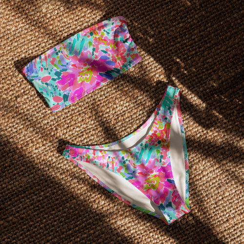 Abstract preppy print recycled bandeau bikini top and V-cut bottoms laid flat on a woven surface