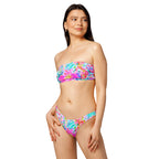 Abstract preppy print recycled bandeau bikini top and V-cut bottoms laid flat on a woven surface