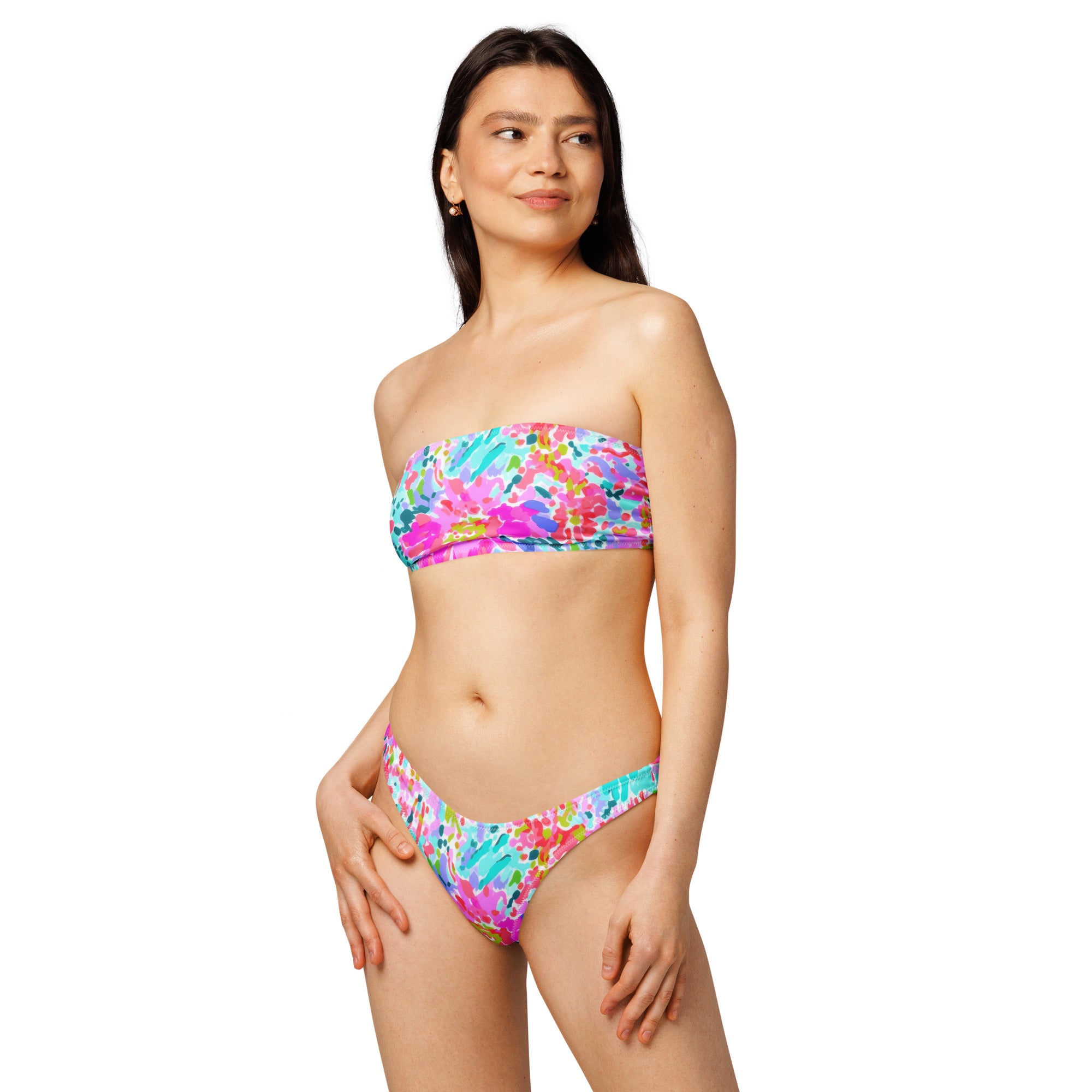 Abstract preppy print recycled bandeau bikini top and V-cut bottoms laid flat on a woven surface