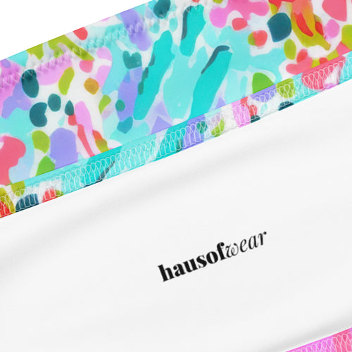 Abstract preppy print recycled bandeau bikini top and V-cut bottoms laid flat on a woven surface